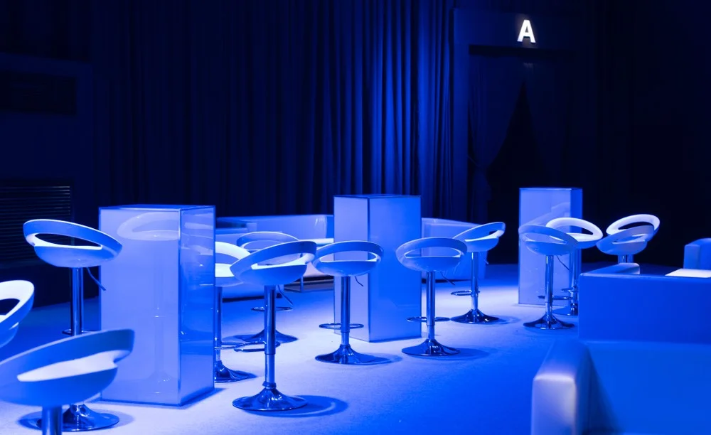 Stylish, blue-lit room with white bar-stools and tables